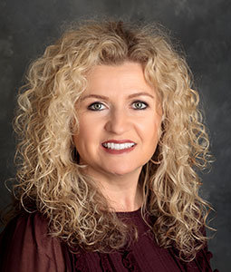 Amanda is pictured from the shoulders up. She has long, blonde, and curly hair and is smiling. 