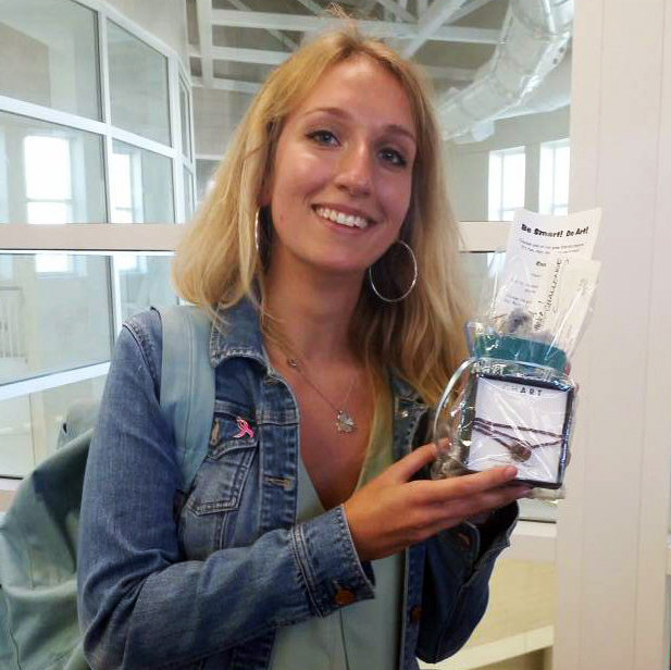 A blonde USC student in a denim jacket is holding her gift certificate and smiling.