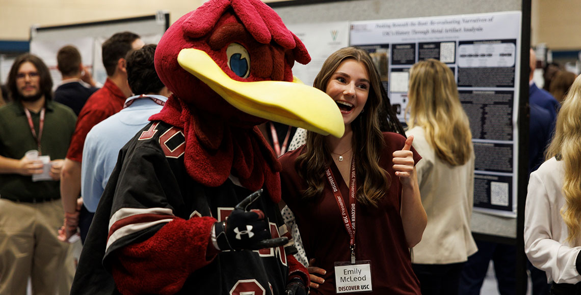 A Discover USC 2026 presenter poses for a photo with Cocky, both giving the spurs up hand signal.
