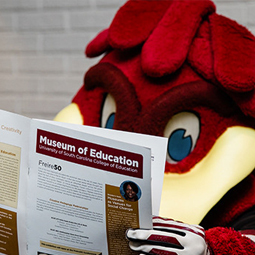 Cocky reading a brochure about USC's Museum of Education
