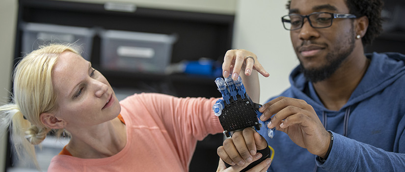 a faculty member fits a student with a robotic arm