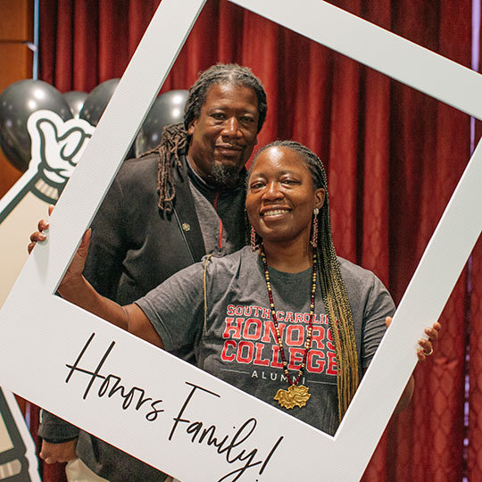 two honors alumni holding up a photo frame that reads, "honors family."