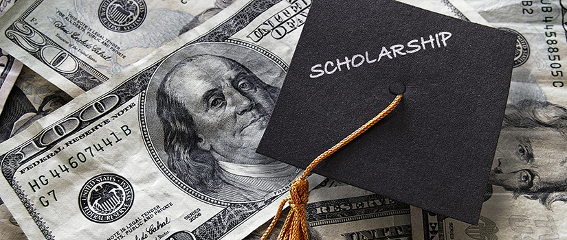 A collection of paper money with a 100 dollar bill prominently featured and a graduation cap on top with the word scholarship written on it.
