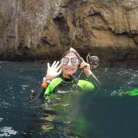 A student waves to the camera with snorkeling gear while swimming in the Galapagos Islands.