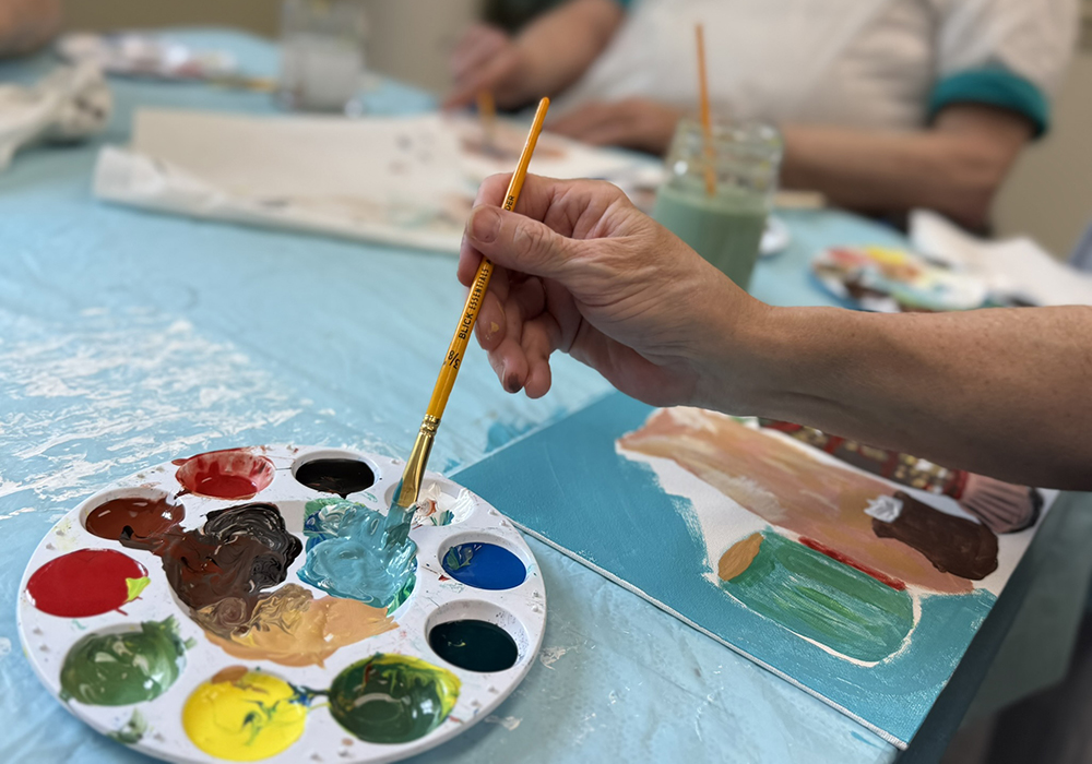 A hand dabs a brush into a palette of paint.