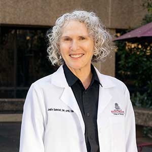 Jennifer Baumstark stands in a white coat outside the College of Nursing at the University of South Carolina. 