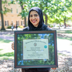 woman stands outside holding a framed award