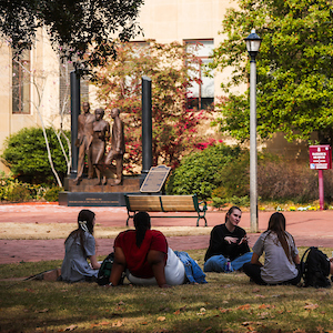 group of students sitting in a circle on the ground in front of a statue 
