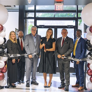 group of people under a garnet and black balloon arch cut a ribbon in a new dining facility